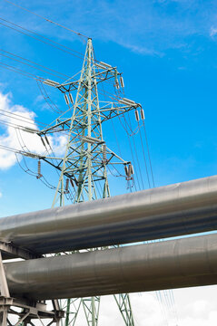 A close-up of a pipeline and a power transmission tower against a blue sky