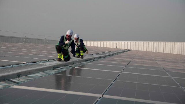 Two engineer inspecting solar panel system on roof building, team worker or technician using walkie talkie check installation solar cell, renewable sustainable, alternative energy power generation.