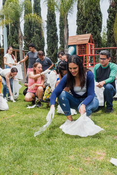 latina woman collecting trash in a public park in Mexico, Latin America. Group of multi age Hispanic volunteers cleaning up and collecting plastic in save the planet and ecology concept