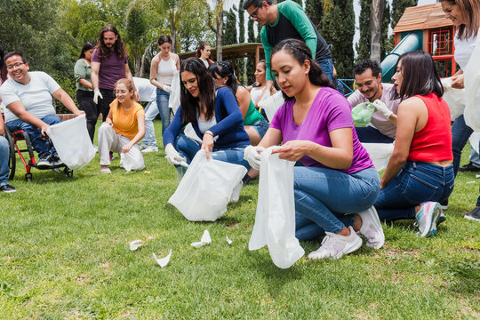 latina woman collecting trash in a public park in Mexico, Latin America. Group of multi age Hispanic volunteers cleaning up and collecting plastic in save the planet and ecology concept