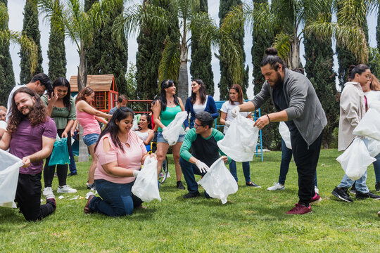 Group of diverse Latin people collecting trash in a public park in Mexico, Latin America. Group of multi age Hispanic volunteers cleaning up and collecting plastic in save the planet concept