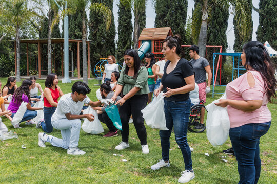 Group of diverse Latin people collecting trash in a public park in Mexico, Latin America. Group of multi age Hispanic volunteers cleaning up and collecting plastic in save the planet concept