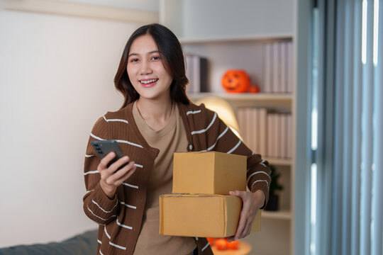 Smiling Asian woman holding delivery boxes and smartphone for online shopping order