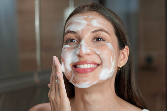 Skincare woman washing face with foaming facewash soap scrub on skin. Face wash exfoliation scrub soap woman washing scrubbing with skincare cleansing product.