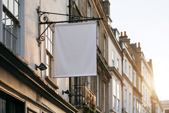 Blank white projecting flag sign on an iron bracket over a city sidewalk
