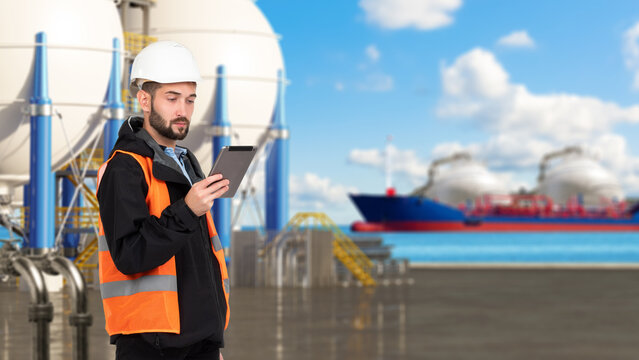 LNG terminal operations. Engineer monitors liquefied natural gas storage and marine loading with a tablet as an LNG tanker stands near the terminal.