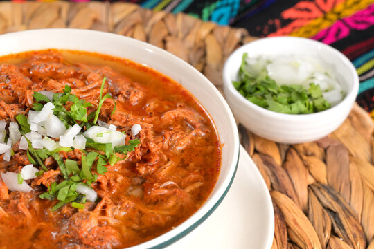Beef birria stew with onion and cilantro in a white bowl to the side