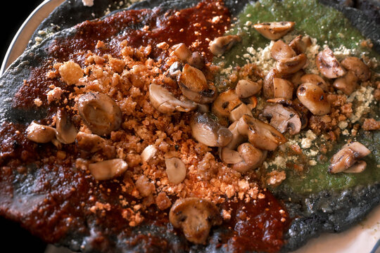 Traditional Mexican blue corn sopes topped with mushrooms, green and red salsa, close up