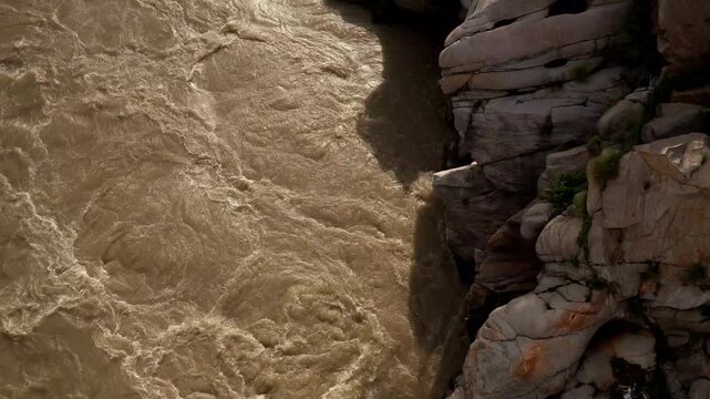 Close-up high-angle video shows the Beas River flowing rapidly beside a rocky riverbank in Mandi, Himachal Pradesh, India, after heavy monsoon rainfall.