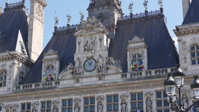 Hotel de Ville facade with clock, statues, and flags under a clear sky