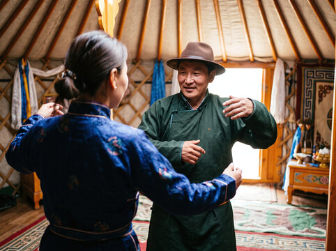 Mongolian couple in traditional deel performing biyelgee dance inside a yurt