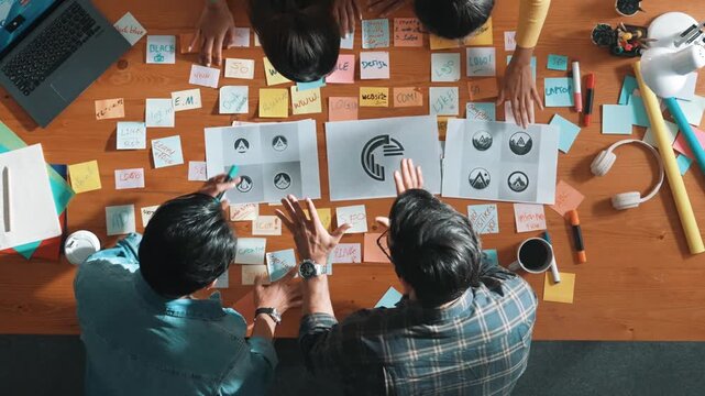 Top view of business team write graphic logo on meeting table with colorful sticky notes and design while explain idea. Project manager sharing idea and explain concept art to smart team. Symposium.