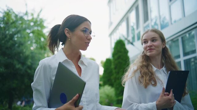 Two business women walking outside with laptops and documents during a workday