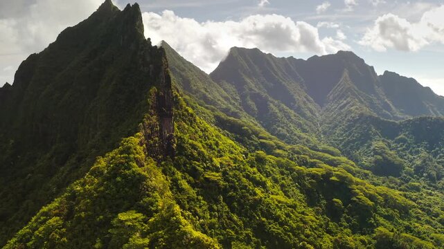 Green volcanic mountains and lush ridges covering the landscape of Moorea island under partly cloudy sky. Wild nature tropical landscape. Travel and explore French Polynesia. Aerial view drone flight