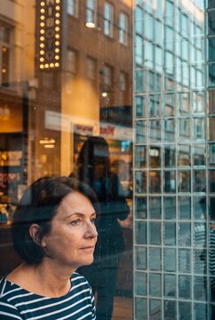 Thoughtful mature woman looking out of a caf&eacute; window with city street reflections on the glass