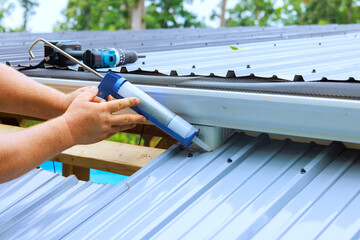 Man applying sealant on metal roof during construction work © ungvar