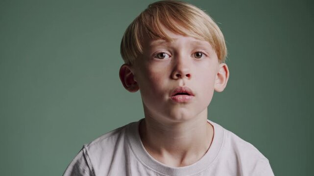 A close-up video shot of a young boy with a thoughtful expression against a green background, capturing an introspective and candid moment.