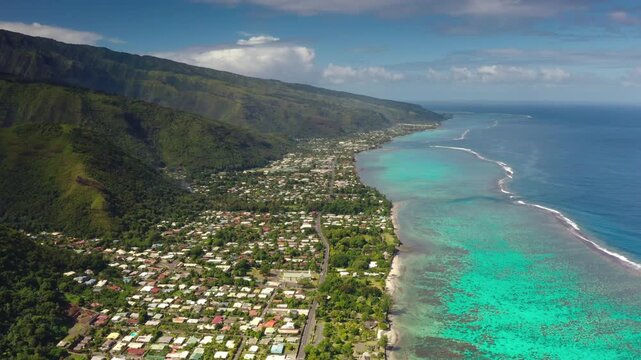 Aerial panorama of Moorea island vibrant coastal town nestled in lush green mountains and sparkling turquoise lagoon coastline, protected by a natural coral reef. Travel and explore French Polynesia
