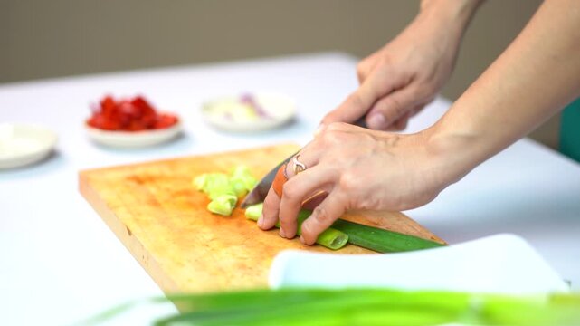 Woman hands slicing fresh green onion on a wooden cutting board