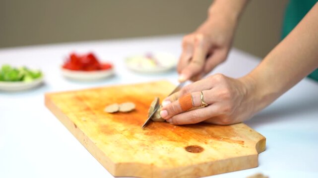 Woman slicing galangal root on a wooden cutting board in the kitchen