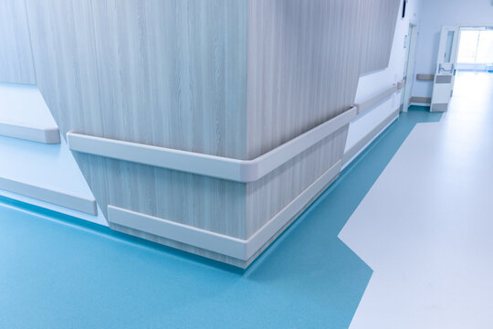 Protective rails wrap the corner of a panelled wall in a bright hospital corridor. The handrail helps patients move to the wards on their own. Barrier free design of a new modern hospital