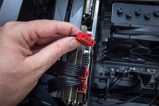 Close up of a hand connecting red modular PCI power connectors to a powerful graphics card inside a PC case. Building or upgrading a powerful gaming PC