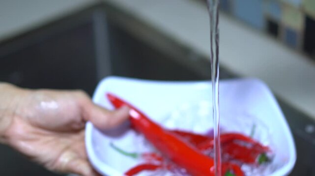 Woman washing red chili peppers and garlic in a white bowl in kitchen