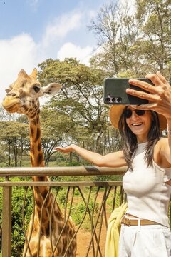 Close up Cheerful female tourist blogger take selfie feeds tall Rothschild giraffe from elevated observation platform, Giraffe Centre Langata Nairobi Kenya eco travel wildlife conservation lifestyle
