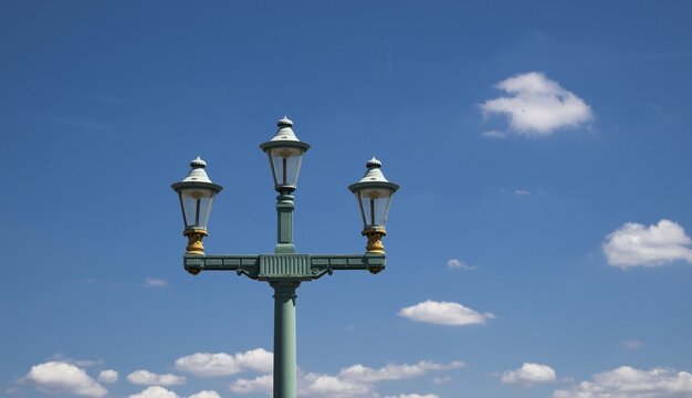 Distinctive historic green cast iron street lamp against blue sky with white sheep clouds, London, England, Great Britain