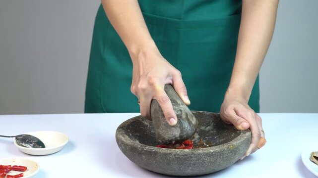 Woman grinding chili peppers and spices using traditional stone mortar and pestle