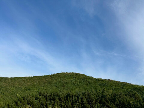 Green hill against blue cloudy sky