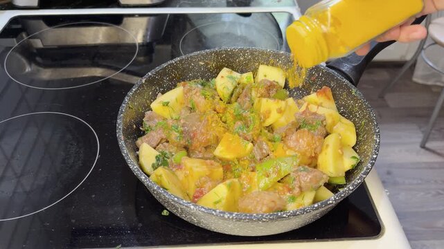 Ground turmeric sprinkled into meat and vegetable stew while cooking in pan.