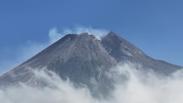 Close Up View of Active Mount Merapi Crater Emitting Volcanic Fumarole Smoke Above Clouds Under Clear Blue Sky