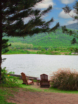 Two Wooden Chairs Facing a Scenic Lake and Mountains in a Lush Green Landscape