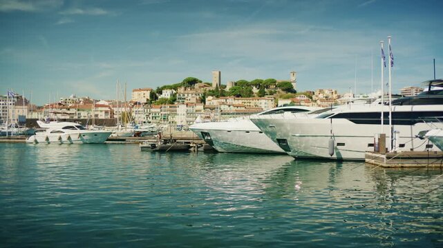 Wide view of sailboats moored in a marina with hillside old town and clock tower behind, Cannes, France