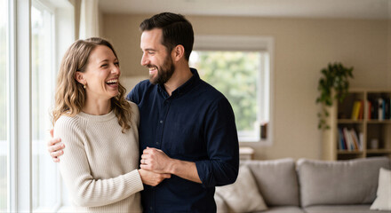 Obraz premium Happy young couple hugging and laughing together while standing in a bright cozy living room
