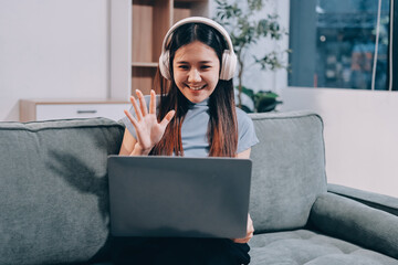 Beautiful young asian woman sitting on sofa and holding joystick playing online video game in living room at house © ARMMY PICCA