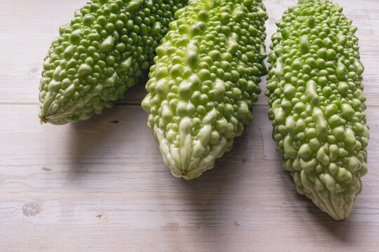 Three fresh bitter melons (goya) arranged on a white wooden table, flat lay with copy space, healthy summer vegetable.
