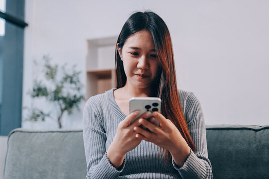 Happy relaxed young woman sitting on couch using cell phone, smiling lady laughing holding smartphone, looking at cellphone enjoying doing online ecommerce shopping in mobile apps or watching videos.