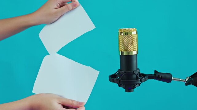 Close-up of hands tearing paper near professional microphone in recording studio setting