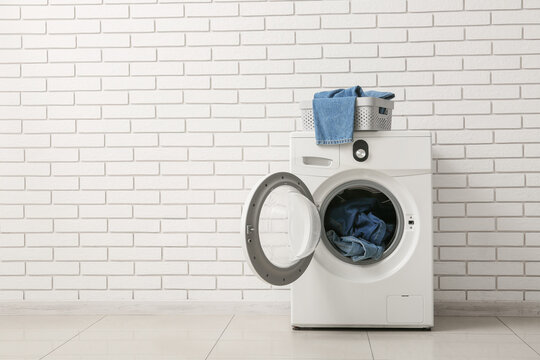 Household chores and laundry day, modern washing machine with denim clothes in a basket against a white brick wall in a home laundry room interior