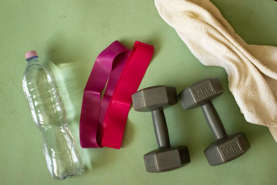 Fitness equipment on green mat top view. Flat lay of dumbbells, resistance bands, water bottle and towel. Home workout gym accessories for weight loss training, copy space.