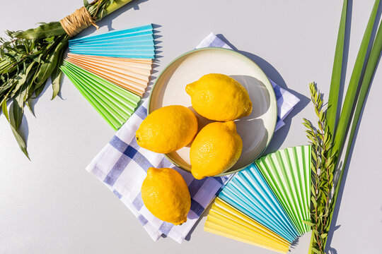 Top view of yellow citrus etrog fruits on a plate, palm and willow branches, bright paper crafts for the holiday of Sukkot. Light background.