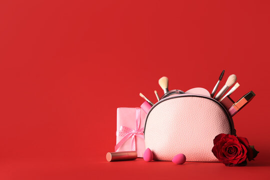 Cosmetic bag with makeup products, beautiful rose and gift box on red background. Valentines day celebration