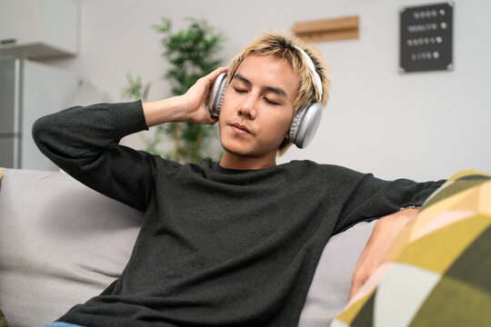 Asian young man wearing wireless headphones while listening to music. 