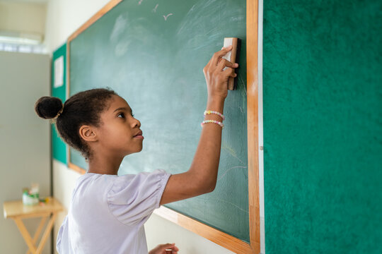 African American student erasing chalk on blackboard in a classroom. 