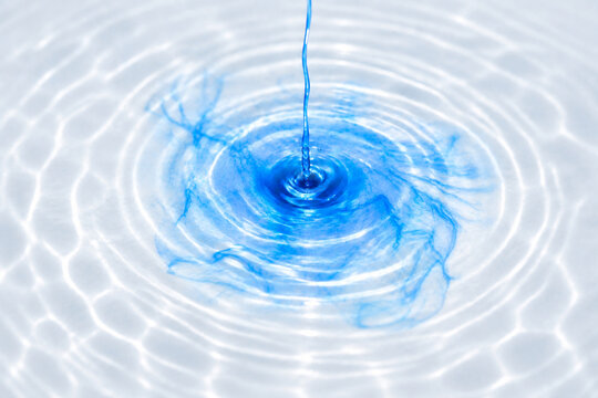 Blue liquid flowing into clear water with expanding ripples