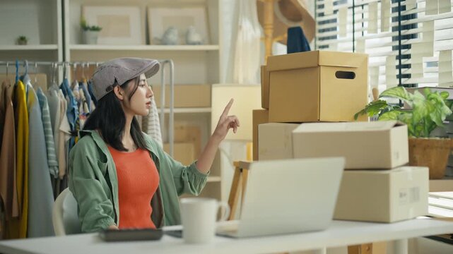 Starting SME Small business entrepreneur,Online business, Work at home concept.Asian business woman using a laptop computer and phone call receive checking customer order online shipping boxes at home
