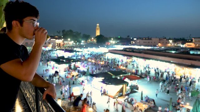 Marrakech, morocco. August 9, 2026. Young man standing on a balcony overlooking the djemaa el fna square in marrakech, morocco, sipping a drink and contemplating the vibrant city