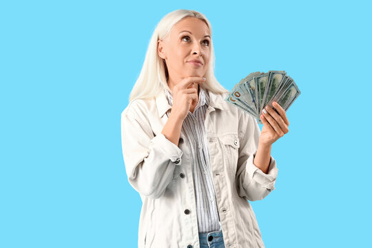 Thoughtful mature woman with dollar banknotes on blue background